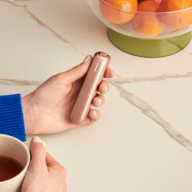 Ploom AURA Rose Gold cihazını tutan el.
