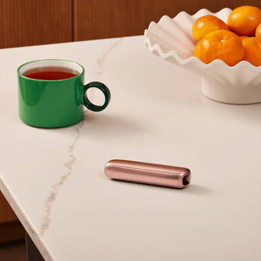 Kahve molası sırasında masada duran Ploom AURA Rose Gold cihazı.
