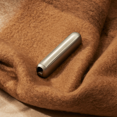 Ploom AURA with a Lunar Silver front panel placed on a maroon blanket
