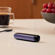 Ploom AURA front panel Lavender device stored on table.

