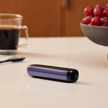 Ploom AURA front panel Lavender device stored on table.
