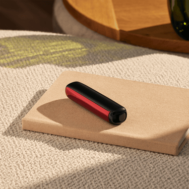 Masa üzerinde cihaza takılı Lava Red renkli Ploom AURA ön panel aksesuarı.