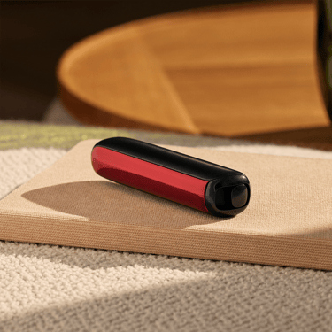 Masa üzerinde cihaza takılı Lava Red renkli Ploom AURA ön panel aksesuarı.

