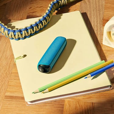 Defter üzerinde duran Ocean Blue arka kapaklı Ploom AURA cihazı
