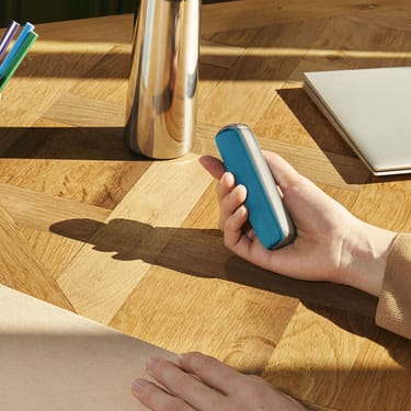 Ocean Blue arka kapak aksesuarına sahip Ploom AURA cihazını tutan bir el
